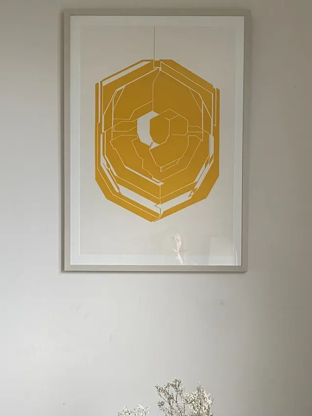 A gold geometric screenprint in a pale wood frame with a wide white mount