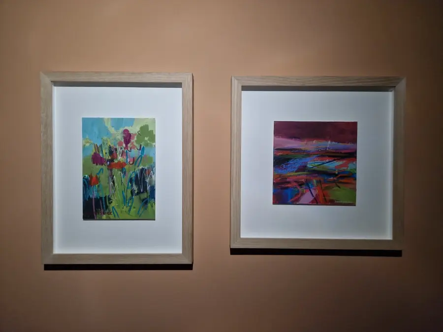 Two framed paintings, a flower meadow and a pink abstract, hung side by side on a warm brown wall